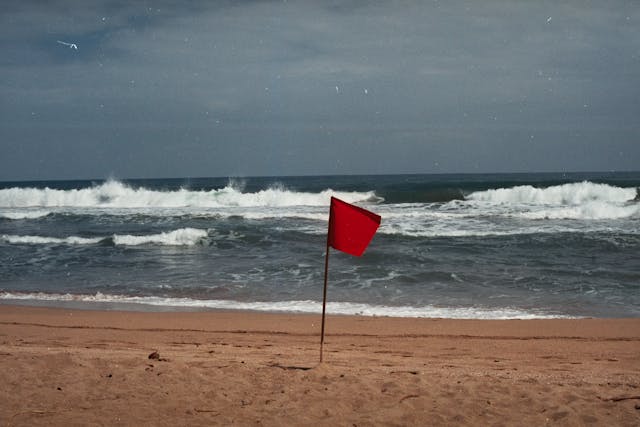 Red warning flag on a sandy beach, signaling dangerous rip current conditions and unsafe swimming.