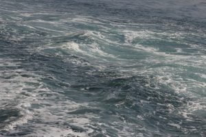 Powerful ocean waves with turbulent white foam, showing the rough surf where rip currents often form.